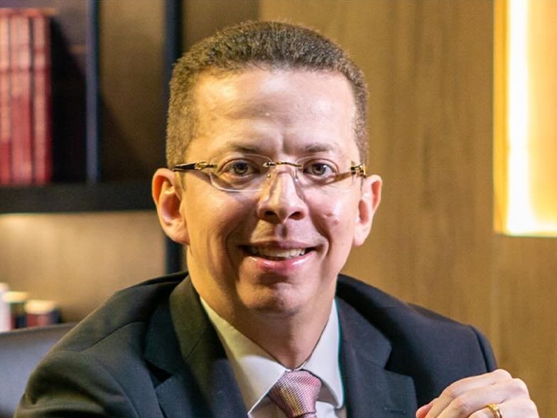 O advogado Alex Noronha de Castro Monte em seu escritório, sorrindo, de terno escuro