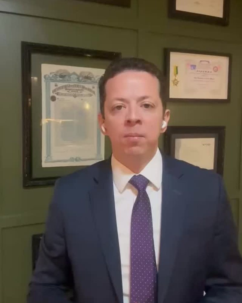 O advogado Alex Noronha em frente à parede de diplomas do escritório